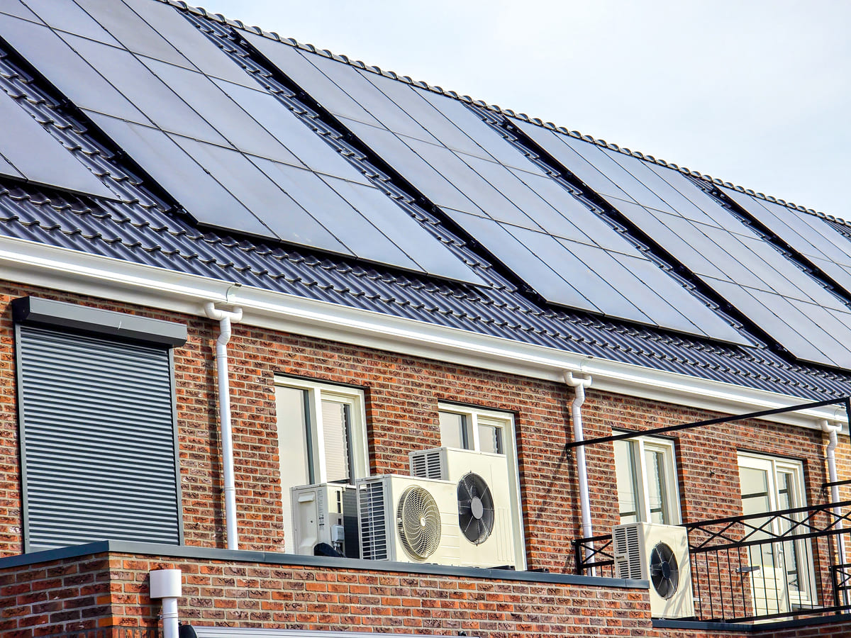 Bomba de calor con aerotermia en el exterior de una vivienda abajo de un tejado con paneles solares